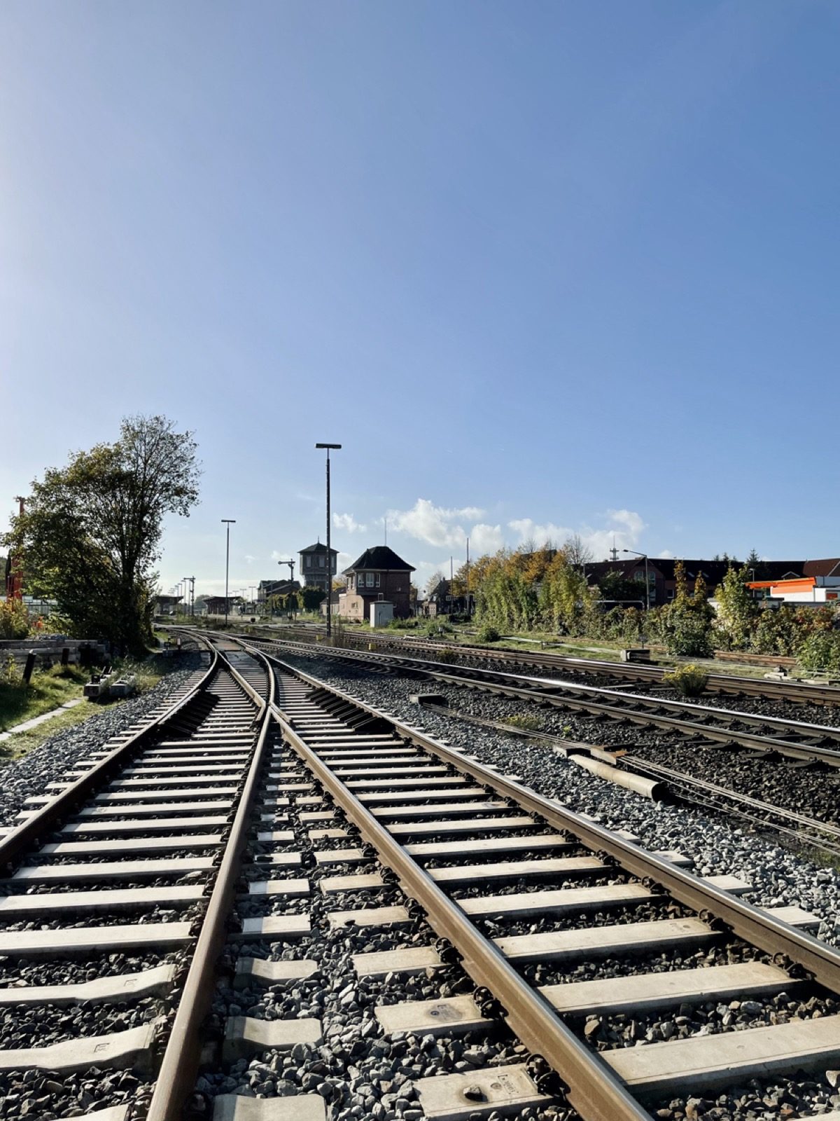 Gleisfeld mit mehreren Weichen, dahinter ein Turmbau, ein Backsteinhaus mit Erker, Beleuchtungsmasten und Wohnhäuser