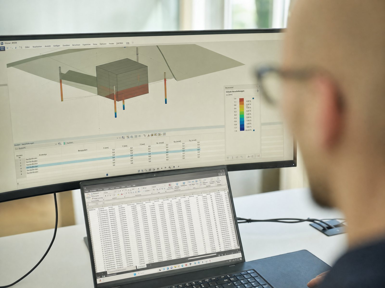 Blick über die Schulter auf ein 3D-Modell eines Bauwerks auf Pfählen mit farbig dargestellten Verschiebungen am Breitbildschirm, davor ein Notebook mit Ergebnistabelle